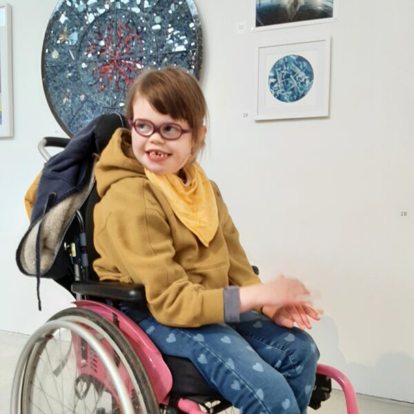 Girl in pink wheelchair smiling in art gallery