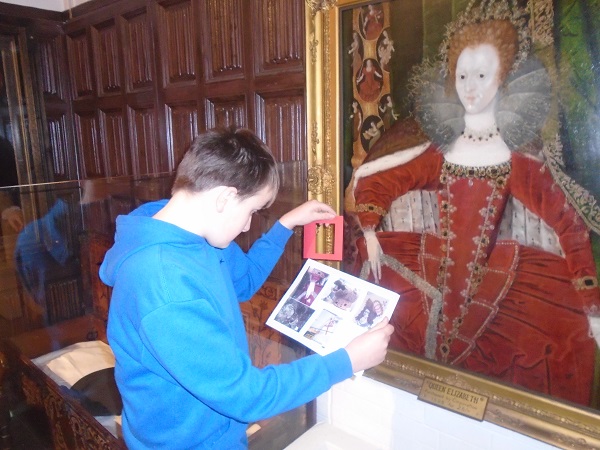 White boy with short brown hair wearing a blue top exploring portrait of a queen through a view finder